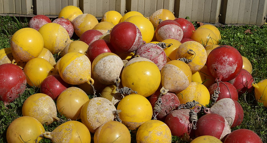 Pile of weathered red and yellow rowing lane buoys on grass