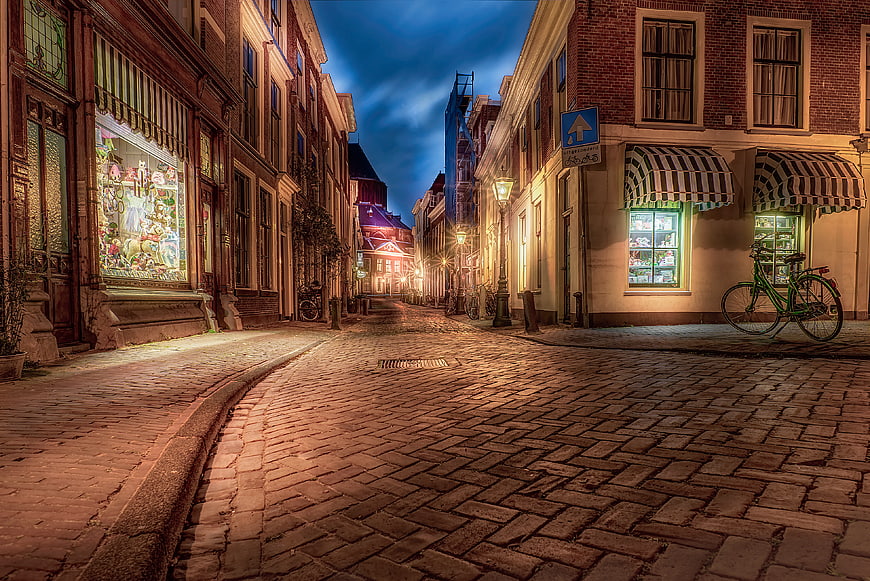 Cobblestone street in Leiden at night with glowing shop windows