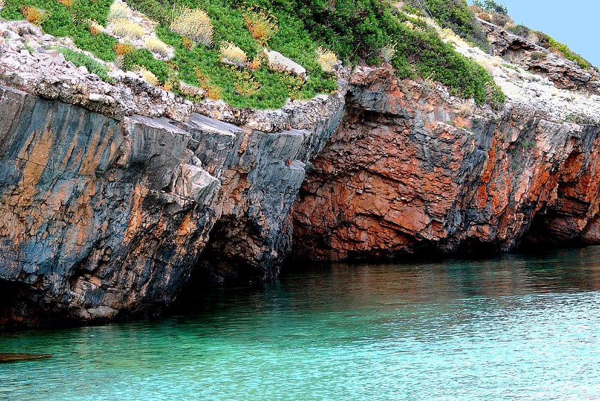Turquoise water meeting rugged coastal cliffs with green vegetation