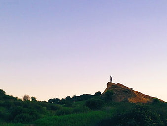 Silhouette of Person Standing on Rocky Hill at Sunset