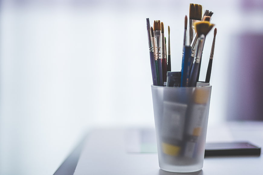 Paintbrushes in frosted glass cup on white desk