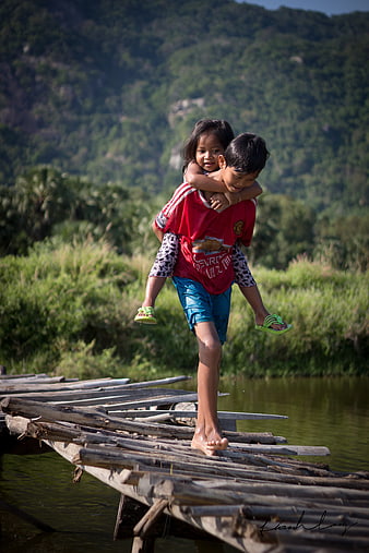 Boy Carrying Sister Piggyback On Rustic Wooden Bridge