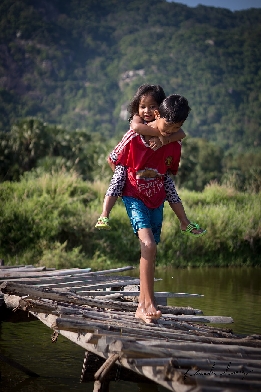 Boy Carrying Sister Piggyback On Rustic Wooden Bridge