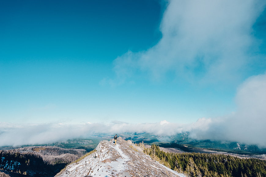 Hiker on Snowy Mountain Peak Above Clouds