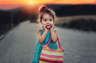 Cute little girl with striped bag on road at sunset