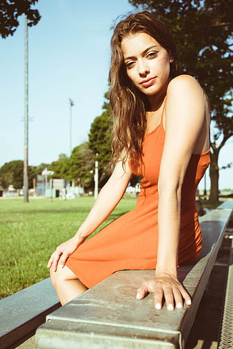 Young woman in orange dress sitting on park bench