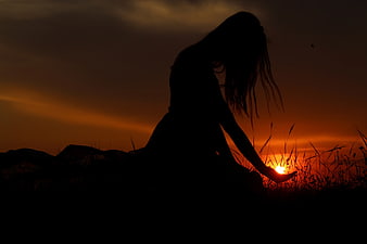 Silhouette of Woman Holding Sun at Sunset