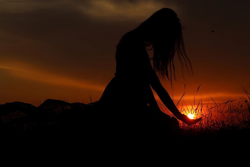 Silhouette of Woman Holding Sun at Sunset