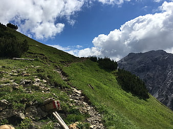 Hiking trail on green mountain slope with rocky peak and blue sky