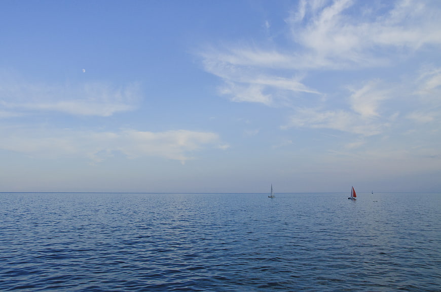 Sailboats on Calm Blue Sea with Moon in Sky