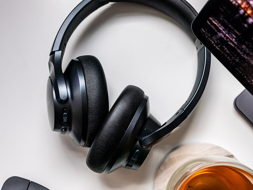 Black Wireless Headphones on White Desk with Smartphone and Drink