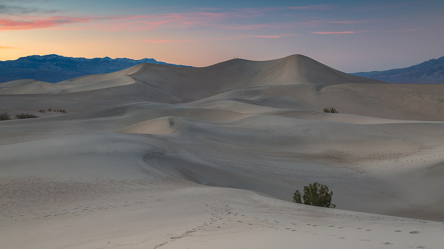 Serene desert sand dunes at sunset with distant mountains