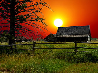 Rustic wooden barn and fence at sunset with dramatic red sky