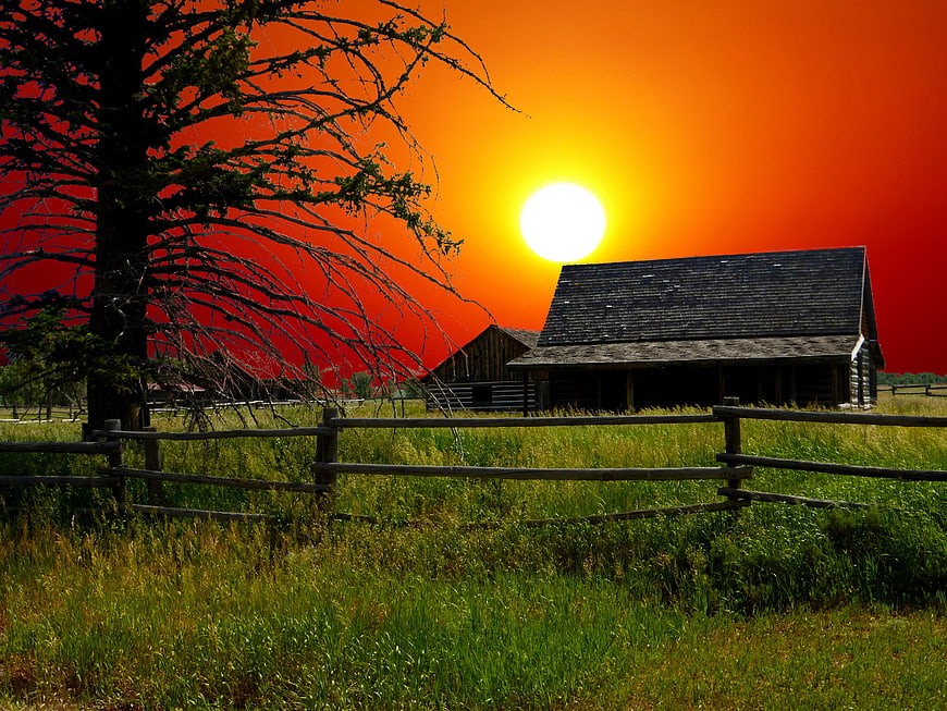 Rustic wooden barn and fence at sunset with dramatic red sky