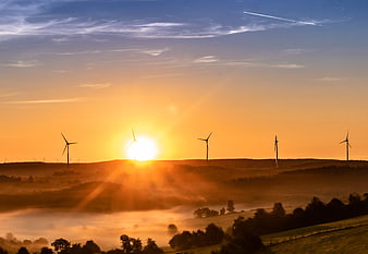 Wind Turbines Silhouetted Against Golden Sunrise Over Misty Hills