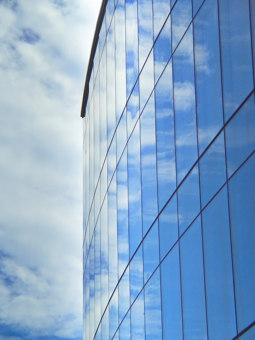 Modern Glass Building Facade Reflecting Blue Sky and Clouds