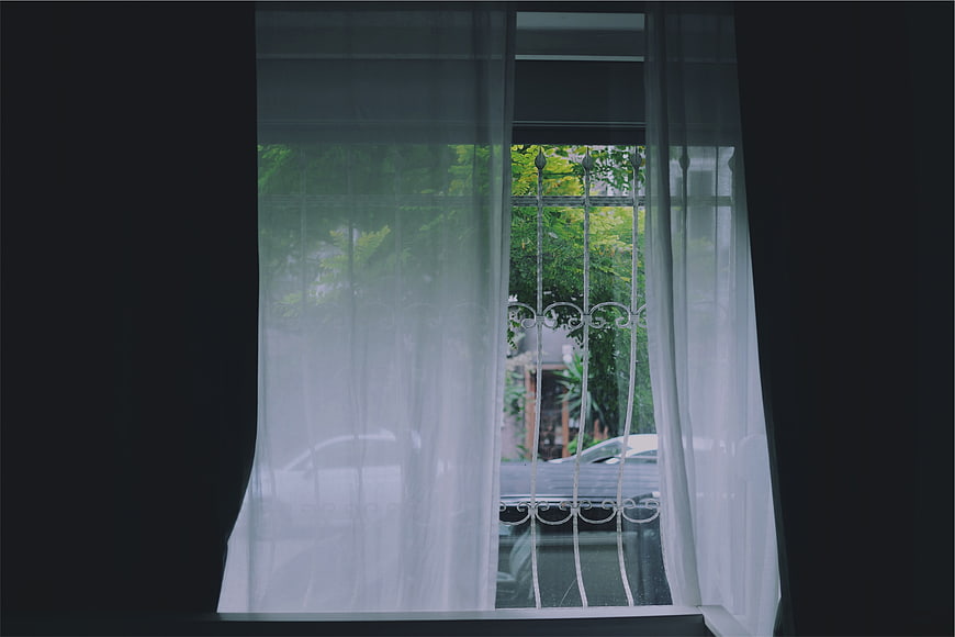 View through sheer white curtains to green trees outside