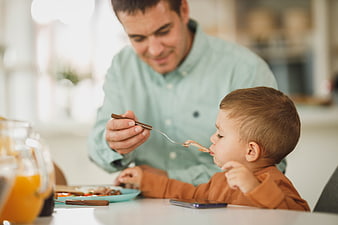 Father feeding toddler son breakfast at home table