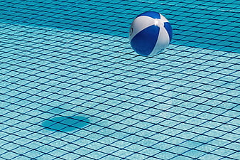 Blue and white beach ball floating on a swimming pool safety net
