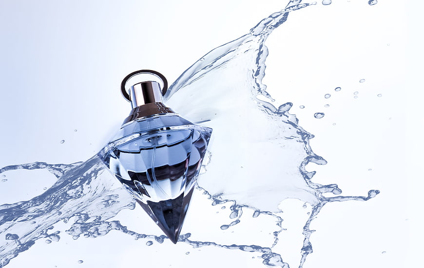 Diamond-shaped perfume bottle with dynamic water splash on white background