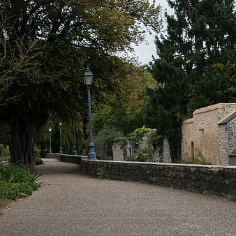 Quiet gravel path in park with stone walls and trees