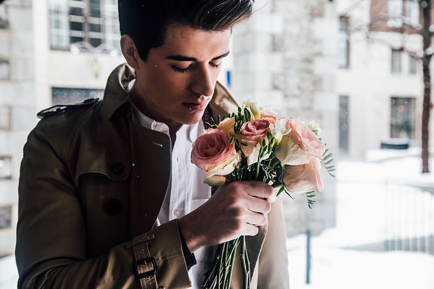 Young man smelling bouquet of pink roses in winter