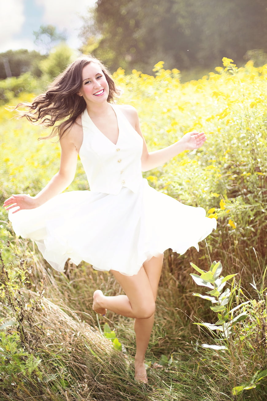 Happy brunette woman dancing barefoot in a sunny yellow flower field