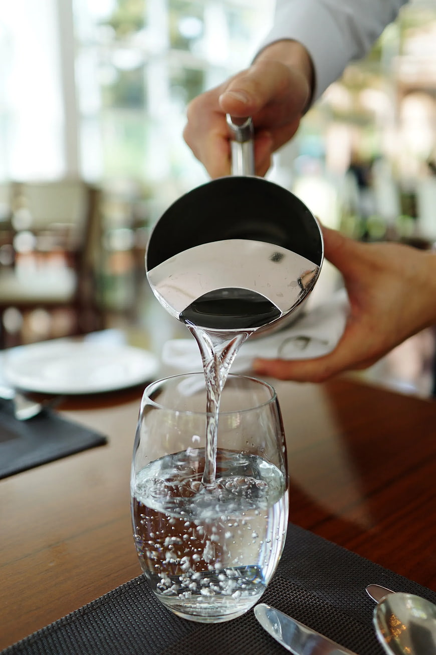 Waiter pouring water into a glass at a restaurant table