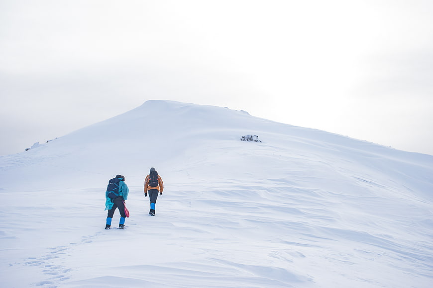 Two hikers climbing a snowy mountain peak in winter