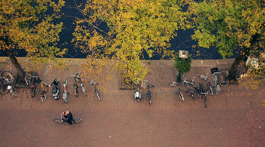 Aerial view of bicycles parked on brick promenade by canal in autumn