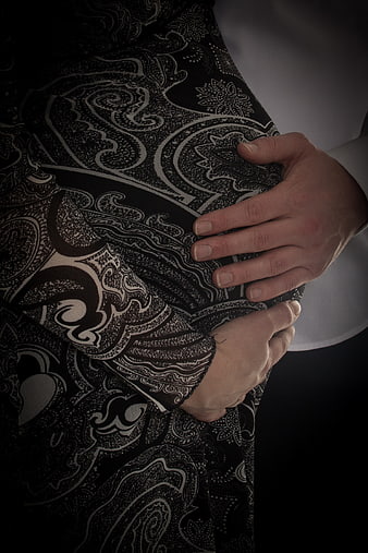 Man's hands gently cradling pregnant woman's patterned belly in dark setting