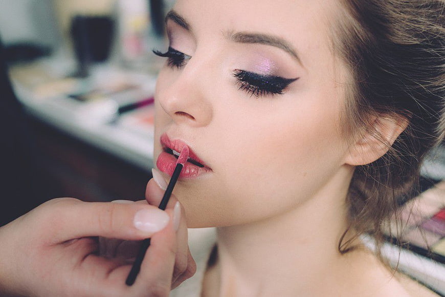 Close-up of woman applying pink lipstick with makeup brush