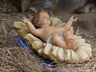 Baby Jesus figurine in nativity scene with straw and lights