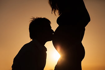 Silhouette of expectant couple kissing at sunset