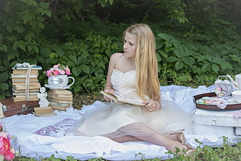 Young woman in white dress reading book during outdoor garden picnic