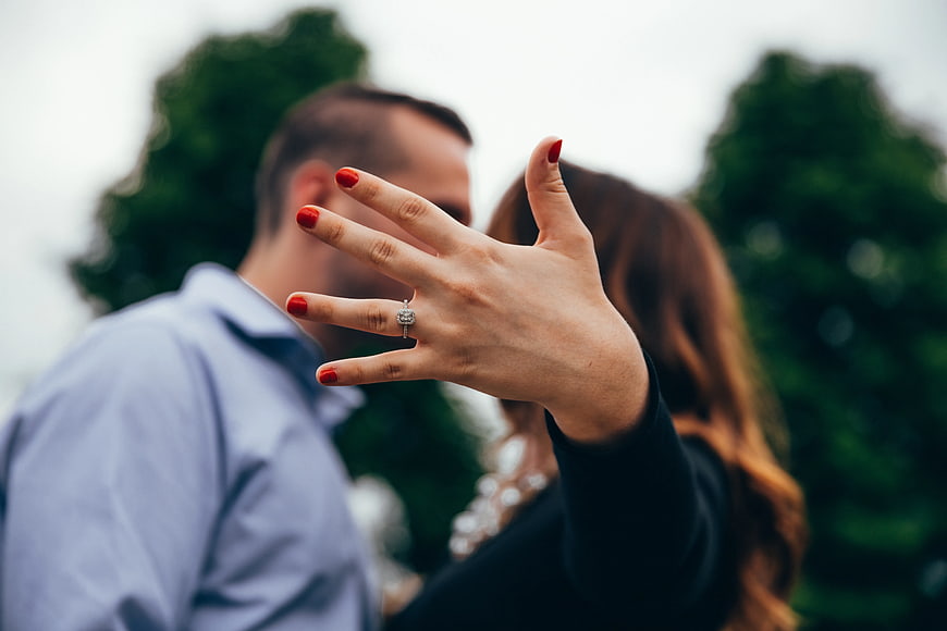 Woman Showing Engagement Ring with Blurred Couple Background