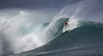 Professional surfer riding a massive turquoise ocean wave with dramatic spray