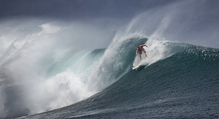 Professional surfer riding a massive turquoise ocean wave with dramatic spray