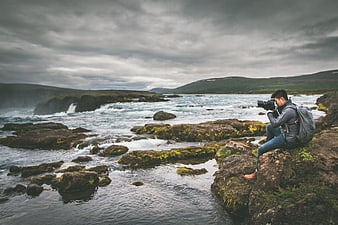 Photographer capturing scenic river landscape with mossy rocks