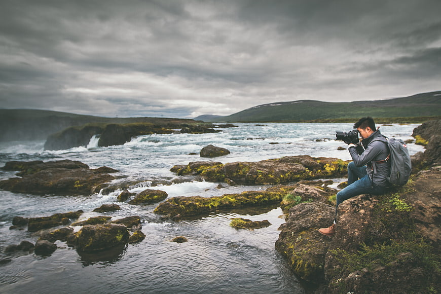 Photographer capturing scenic river landscape with mossy rocks