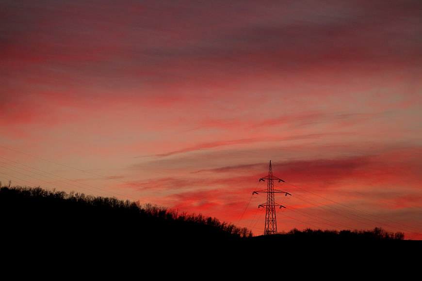 Silhouette of Power Line Tower Against Vibrant Red Sunset Sky