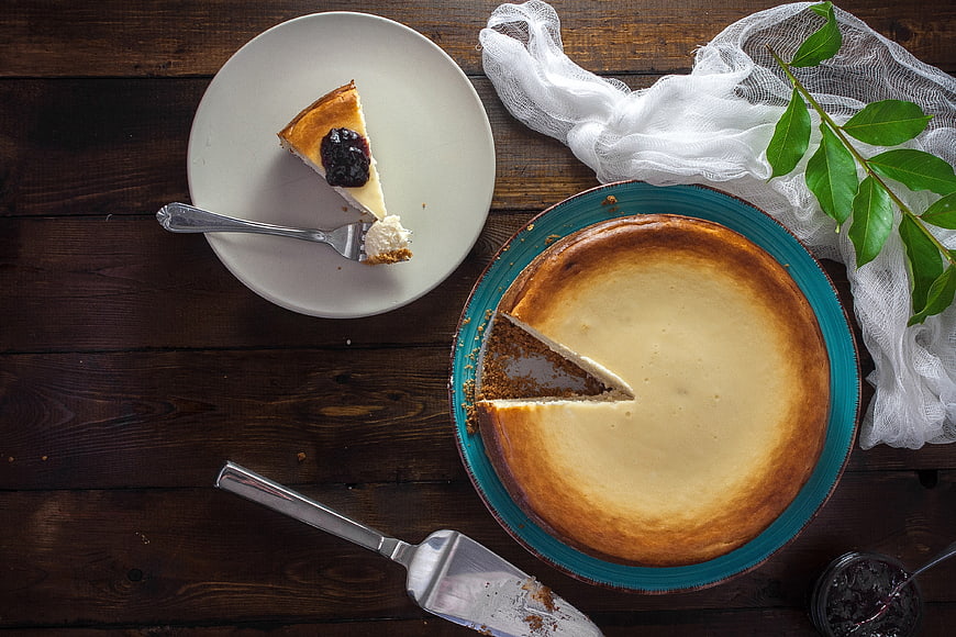 Overhead View of Cheesecake with Slice on Plate and Wooden Table