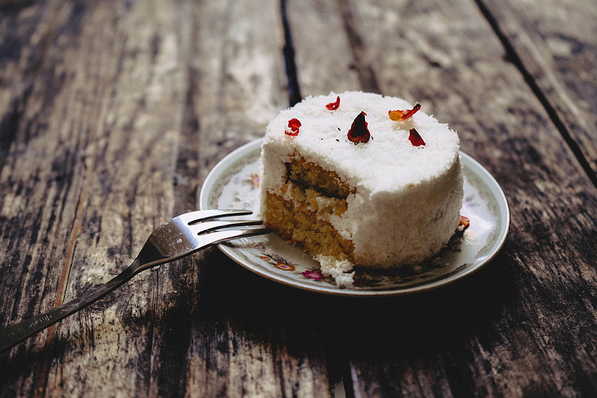 Slice of White Cake with Dried Rose Petals on Rustic Wood