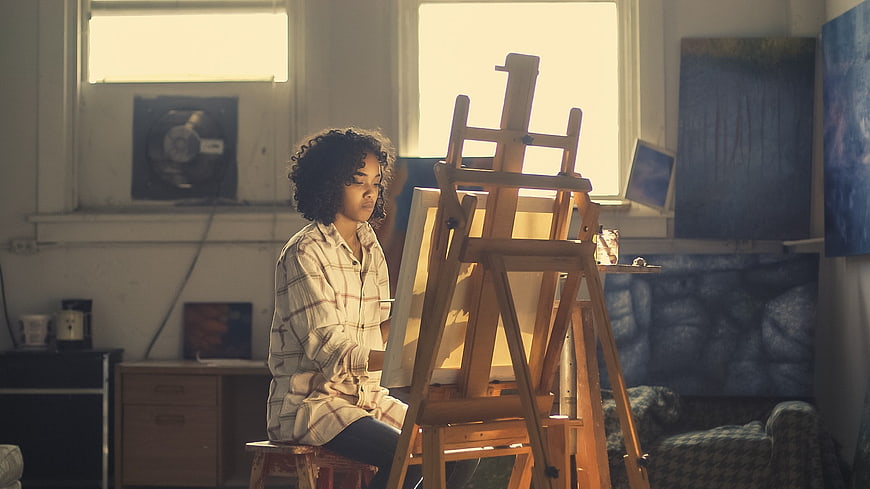 Young female artist painting in sunlit studio