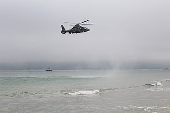 Military helicopter flying low over ocean waves on foggy day