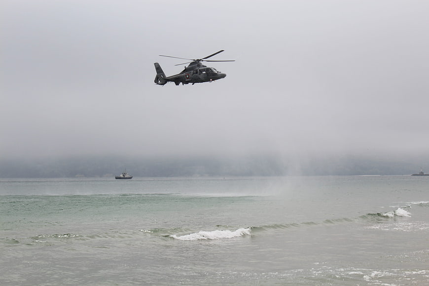 Military helicopter flying low over ocean waves on foggy day
