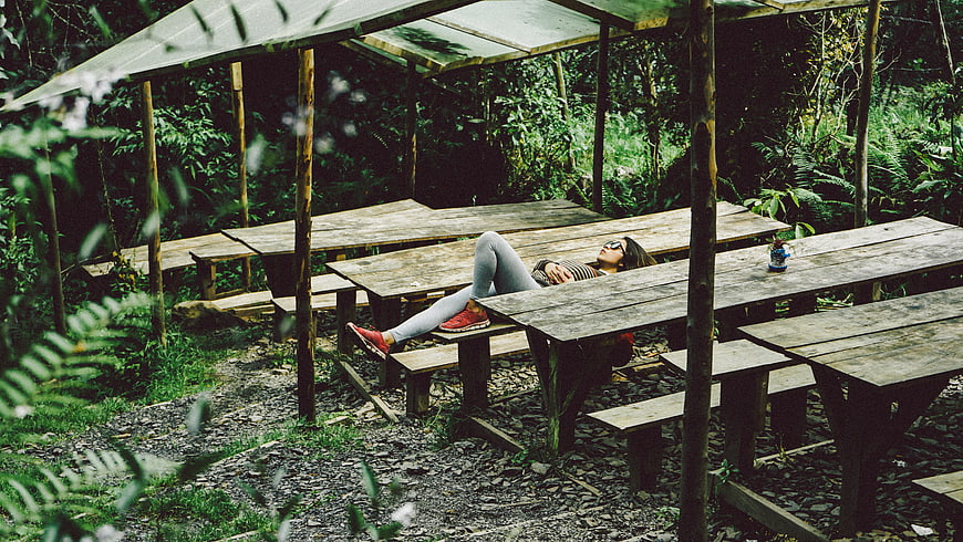 Woman relaxing on wooden picnic table in lush forest