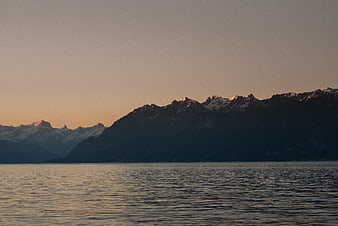 Snow-capped mountains at dusk over calm lake water