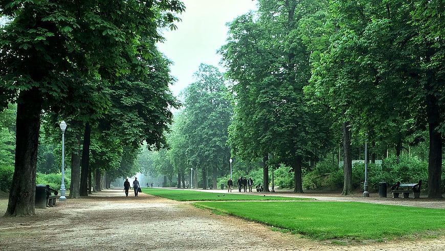 Wide gravel path in green park with trees and people walking