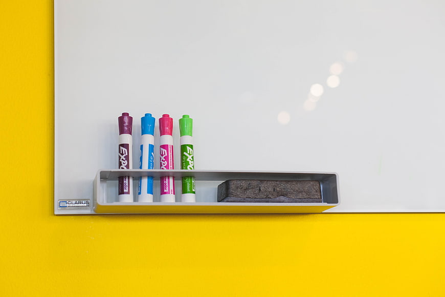 Whiteboard with colorful markers and eraser on yellow wall